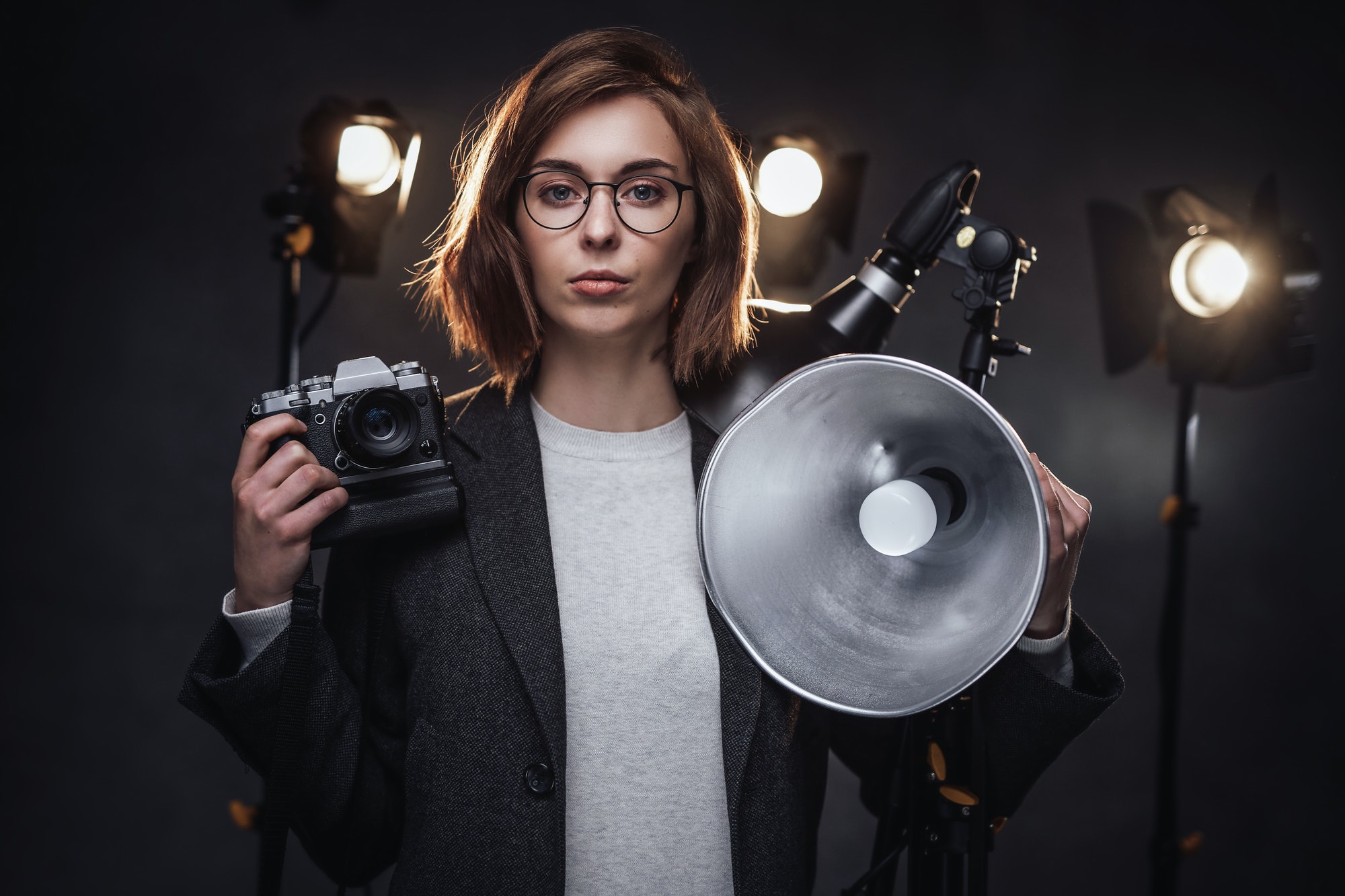 Beautiful redhead female photographer holds a digital camera and looking on the camera