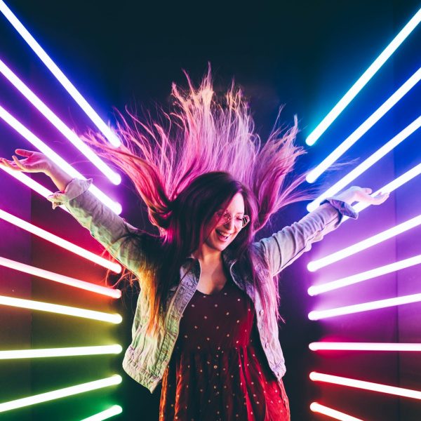 Attractive dancing girl, hair flying, neon light. Portrait of girl posing with hands up.