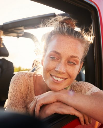 Millennial white couple on a road trip driving in open top car, women leaning on car door, close up